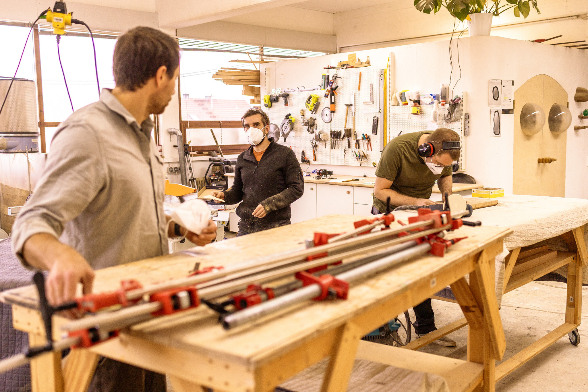 Teilnehmende arbeiten mit Holz und Schraubzwingen an Werkbänken in einem Kurs.