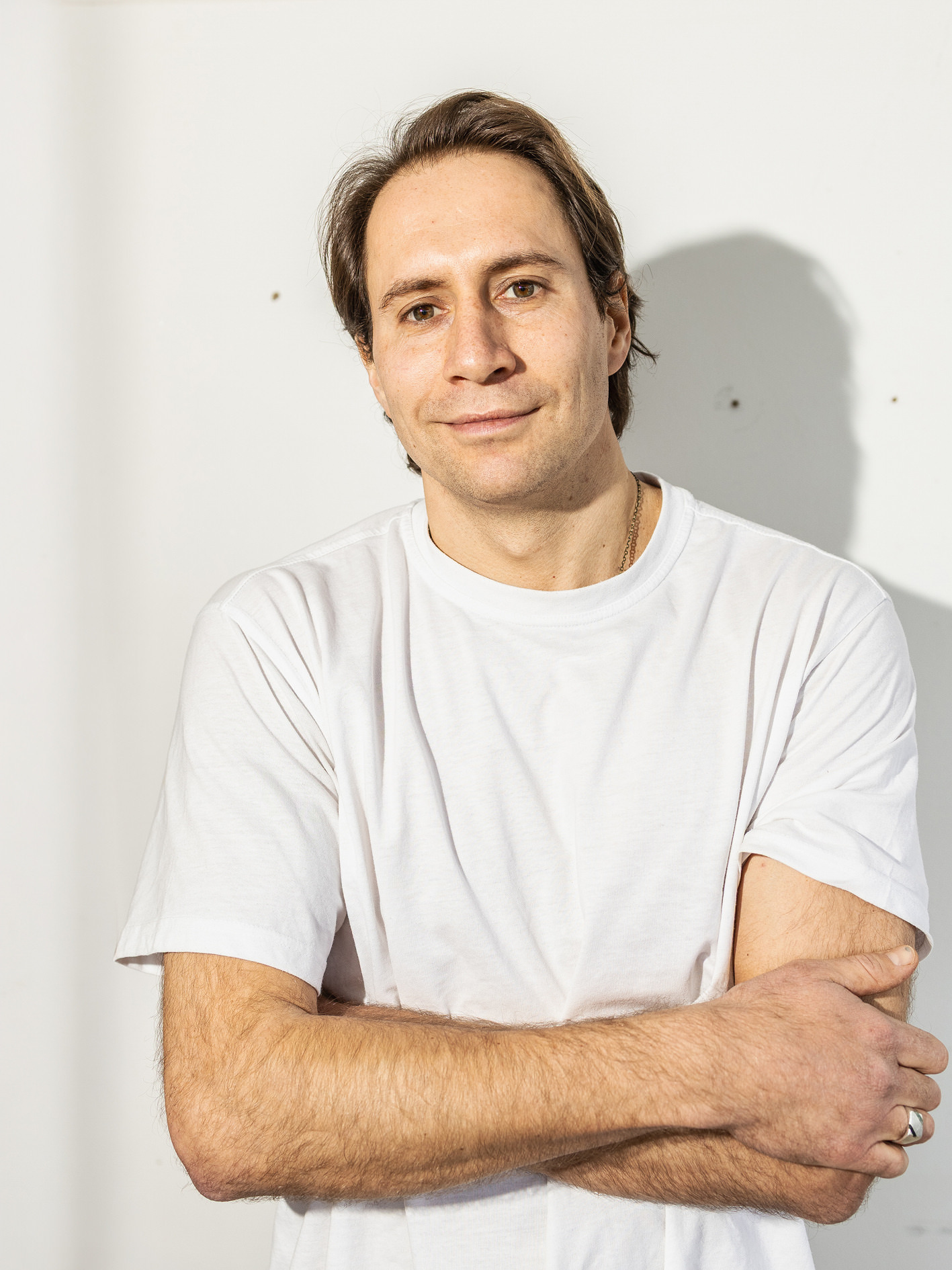 Porträt von Alexander Knysch im weißen T-Shirt vor einer hellen Wand.