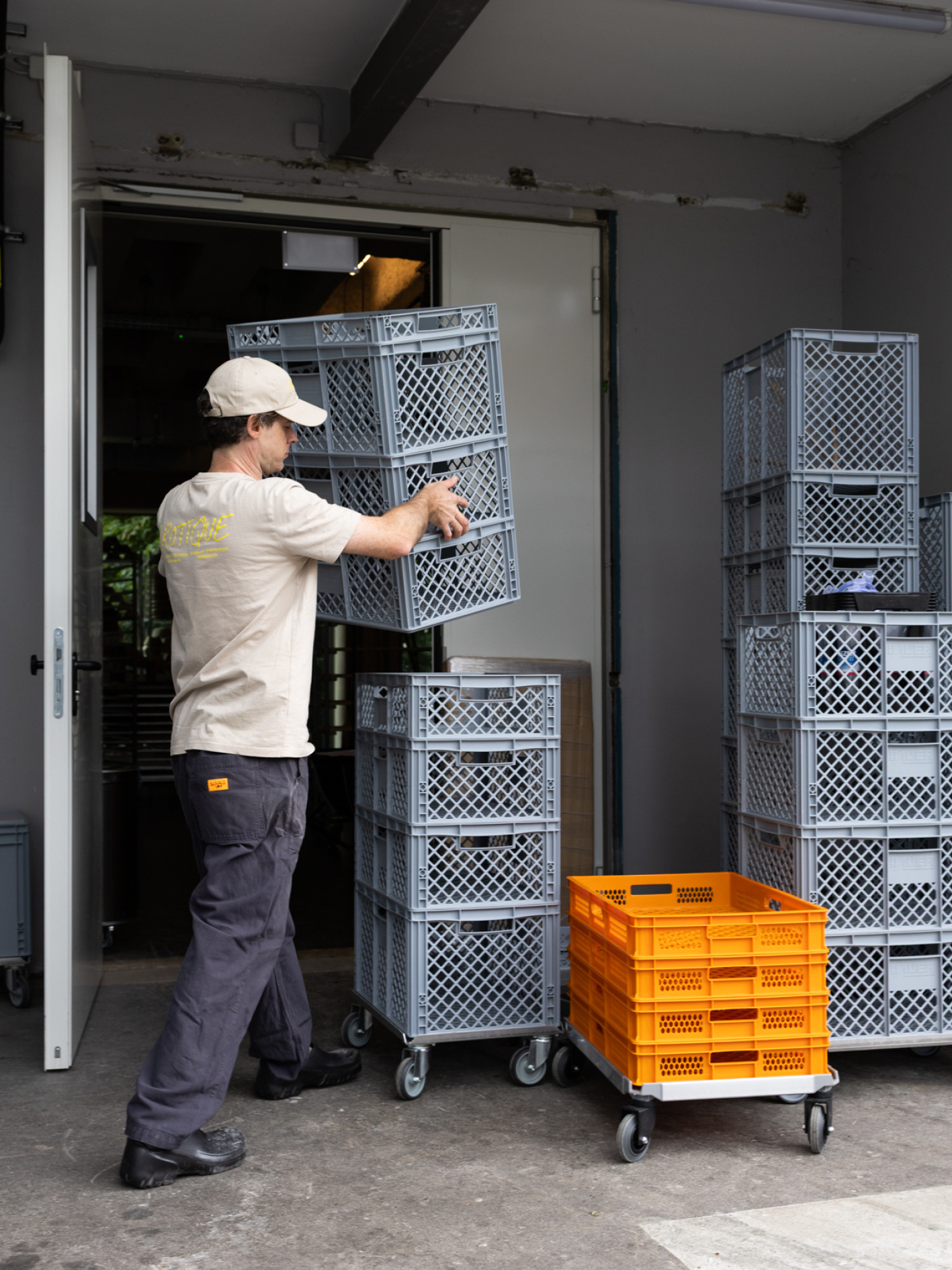 Ein Mitarbeiter bewegt einen hohen Stapel grauer Transportkisten im Eingang der Brotique.