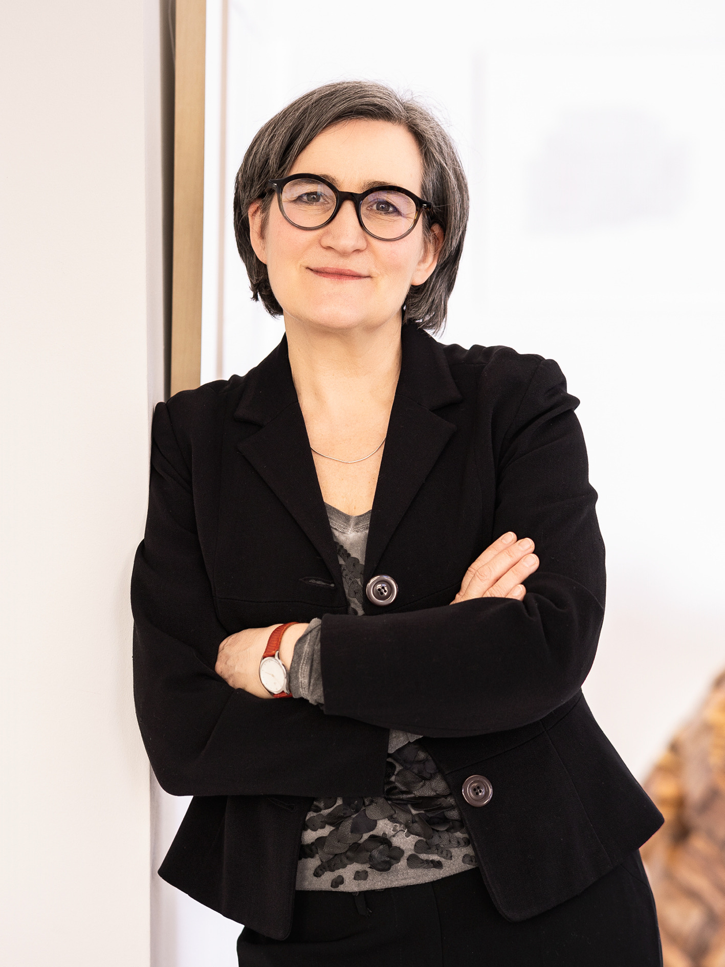 Imke Valentien steht mit verschränkten Armen und schwarzem Blazer in ihrer Galerie.