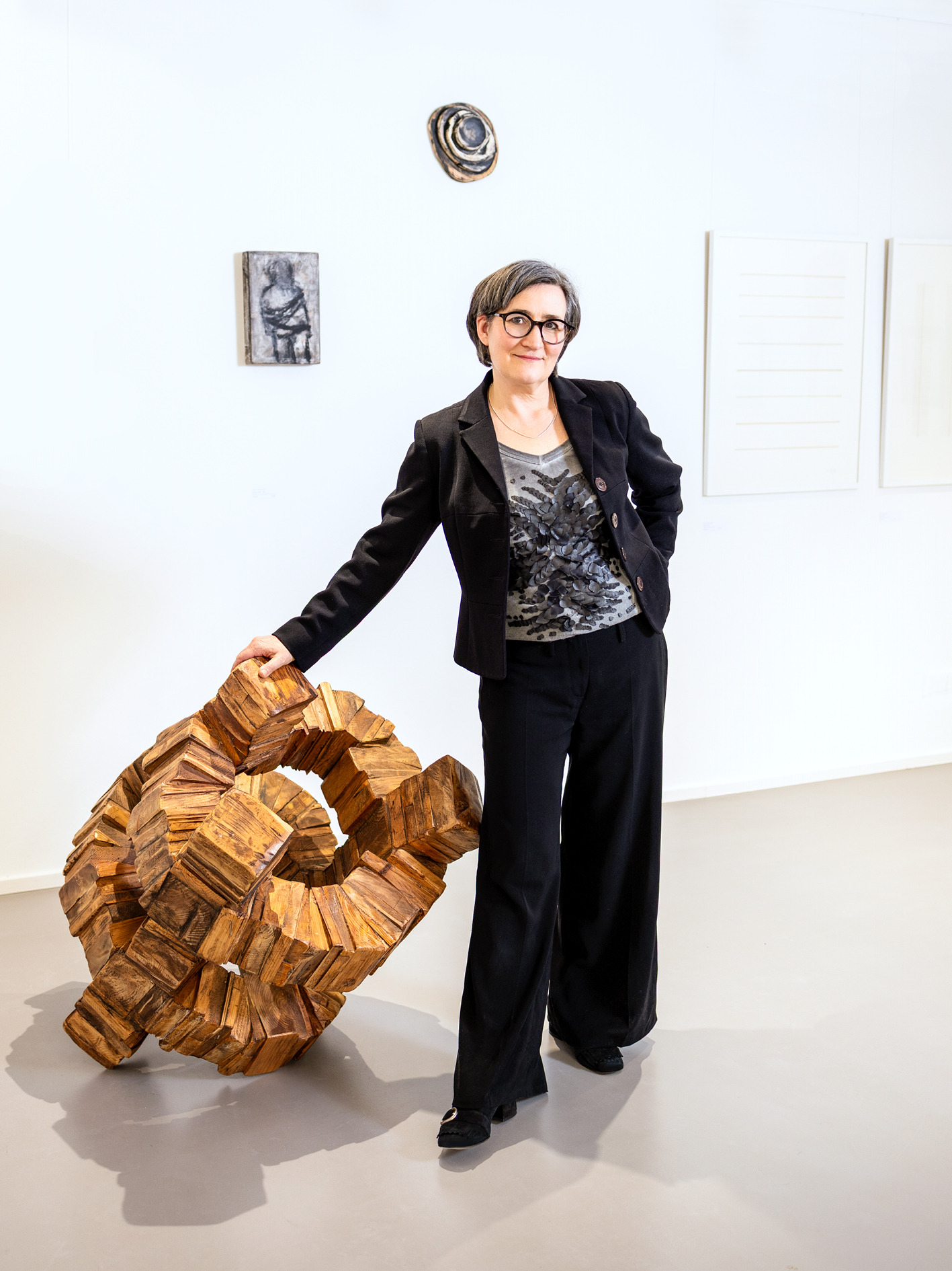 Imke Valentien steht neben einer Holzskulptur vor Kunstwerken in ihrer Galerie.