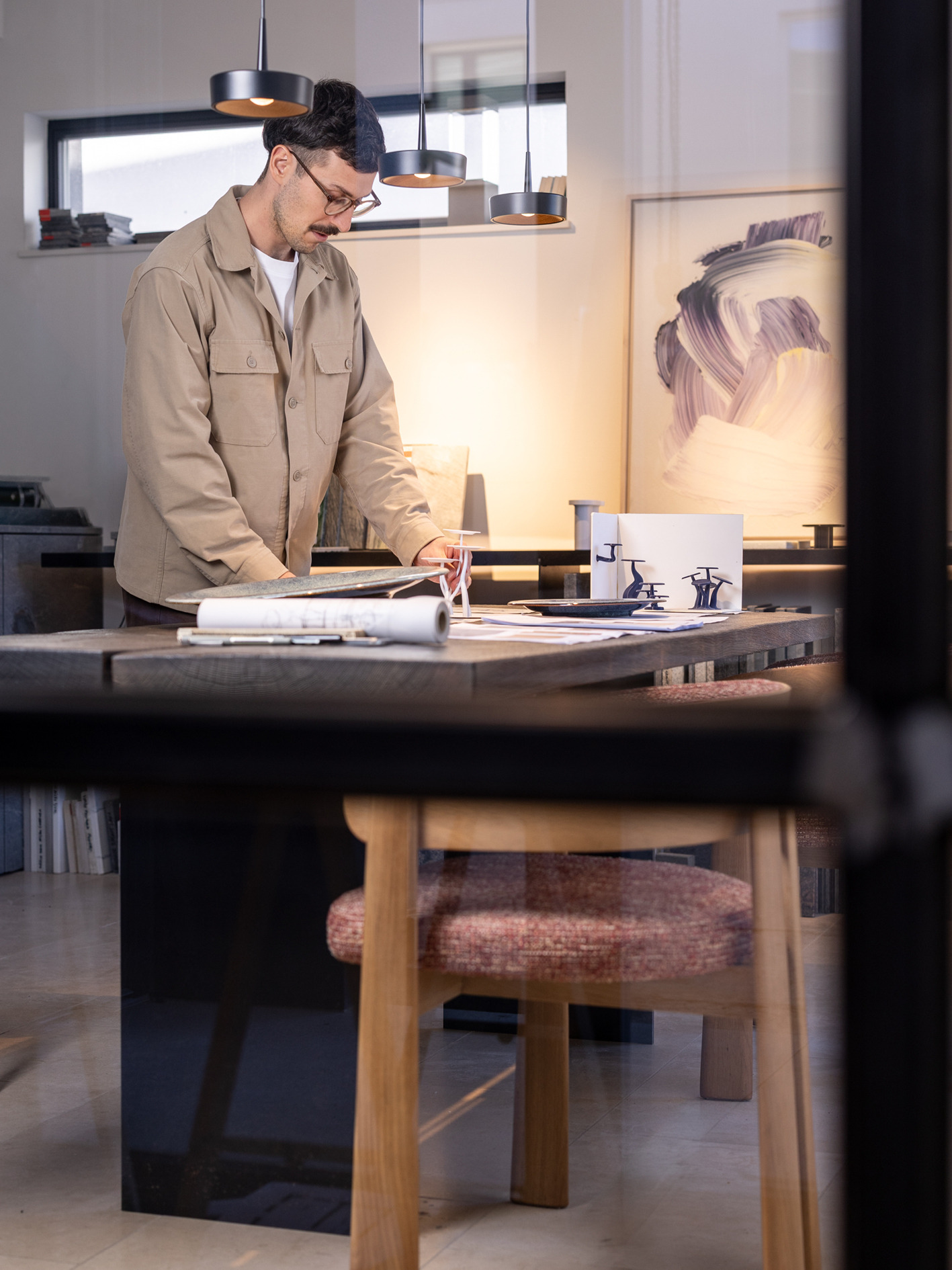 Ein Designer arbeitet an einem Tisch mit Modellen, Zeichnungen und Materialmustern.