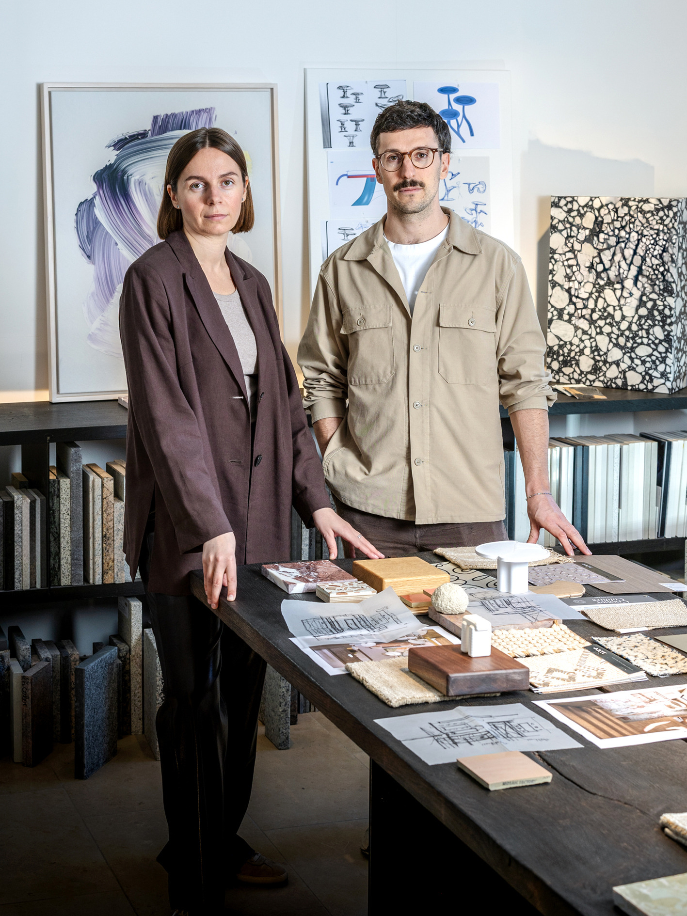 Inna und Marius stehen hinter einem mit Materialproben und Zeichnungen belegten Tisch.