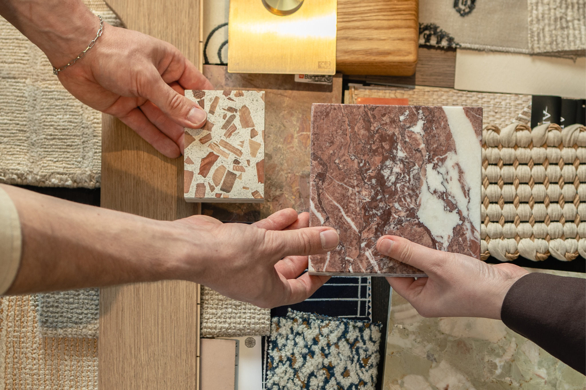 Hände vergleichen zwei Steinmuster über einer Auswahl aus Holz, Metall und Textilien.