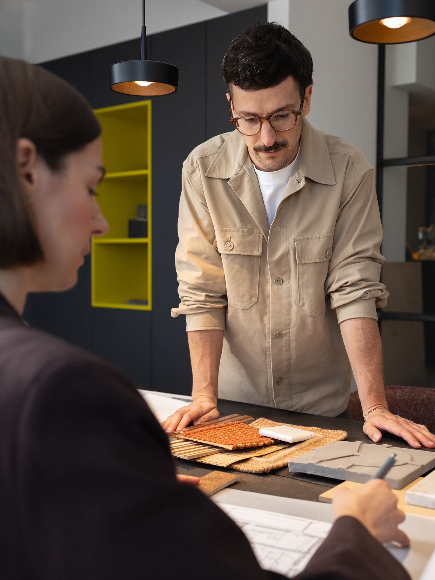 Ein Designer bespricht am Tisch Materialmuster und einen Entwurf mit einer Kollegin.