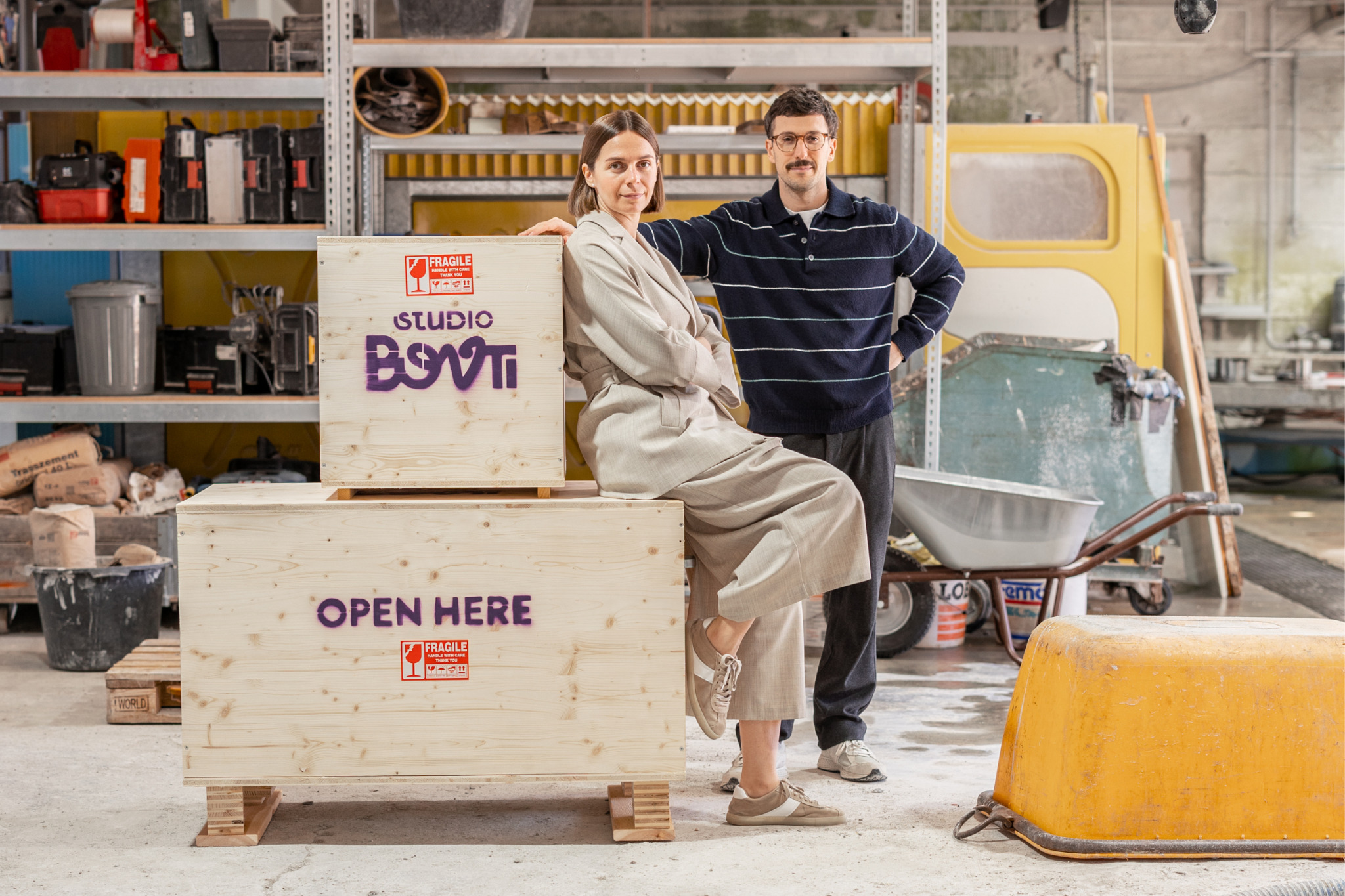 Inna und Marius neben Holzkisten mit dem Schriftzug Studio Bovti in einer Werkstatt.