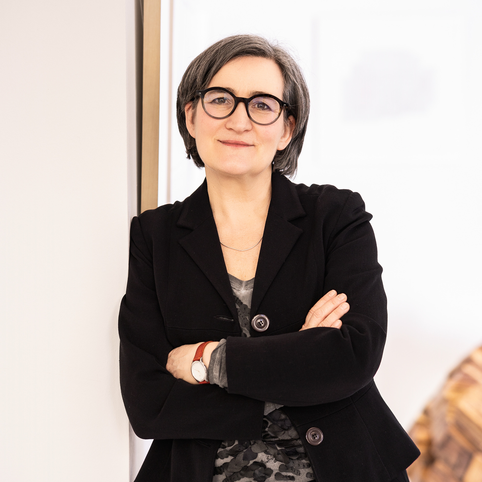 Imke Valentien steht mit verschränkten Armen und schwarzem Blazer in ihrer Galerie.